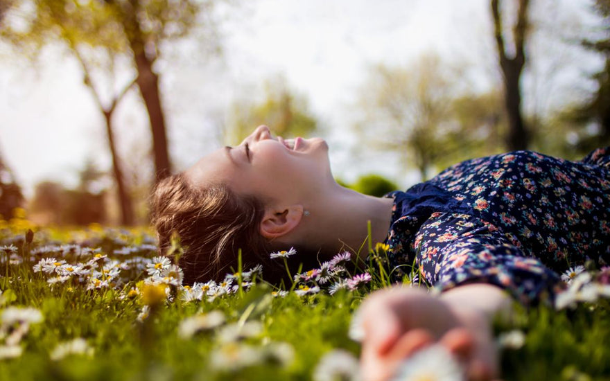 Young woman laying in the grass smiling and soaking up the sun. 