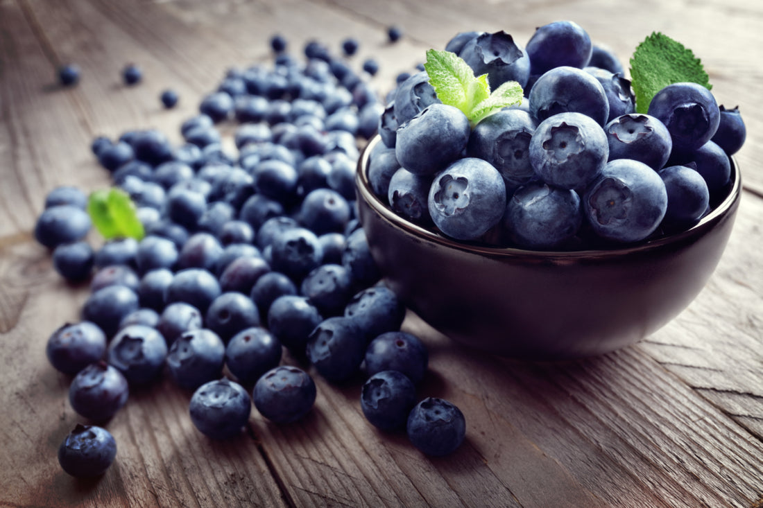 A bowl of blueberries sitting on a wooden tabletop.