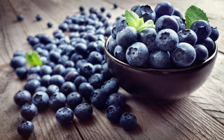 A bowl of blueberries sitting on a wooden tabletop.