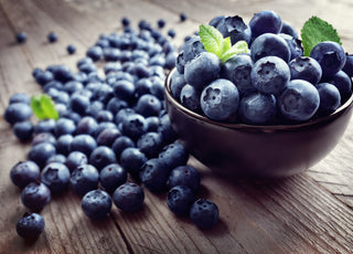 A bowl of blueberries sitting on a wooden tabletop.