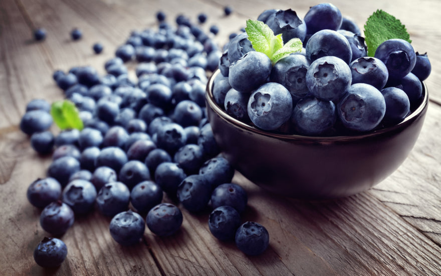 A bowl of blueberries sitting on a wooden tabletop.