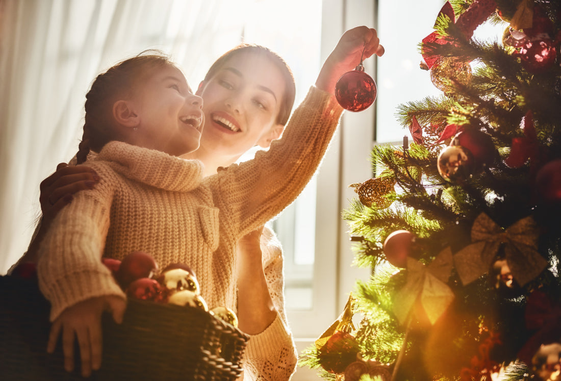 Mother and daughter in matching sweaters smiling while hanging ornaments on the Christmas tree together.
