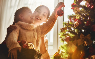 Mother and daughter in matching sweaters smiling while hanging ornaments on the Christmas tree together.