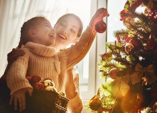 Mother and daughter in matching sweaters smiling while hanging ornaments on the Christmas tree together.