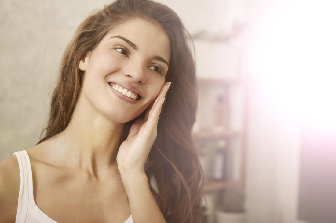 Woman in a white tank top holding her fingertips to her cheek while smiling.