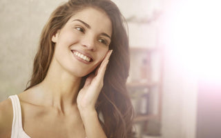 Woman in a white tank top holding her fingertips to her cheek while smiling.