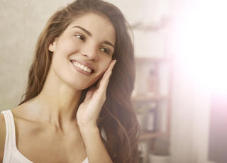 Woman in a white tank top holding her fingertips to her cheek while smiling.