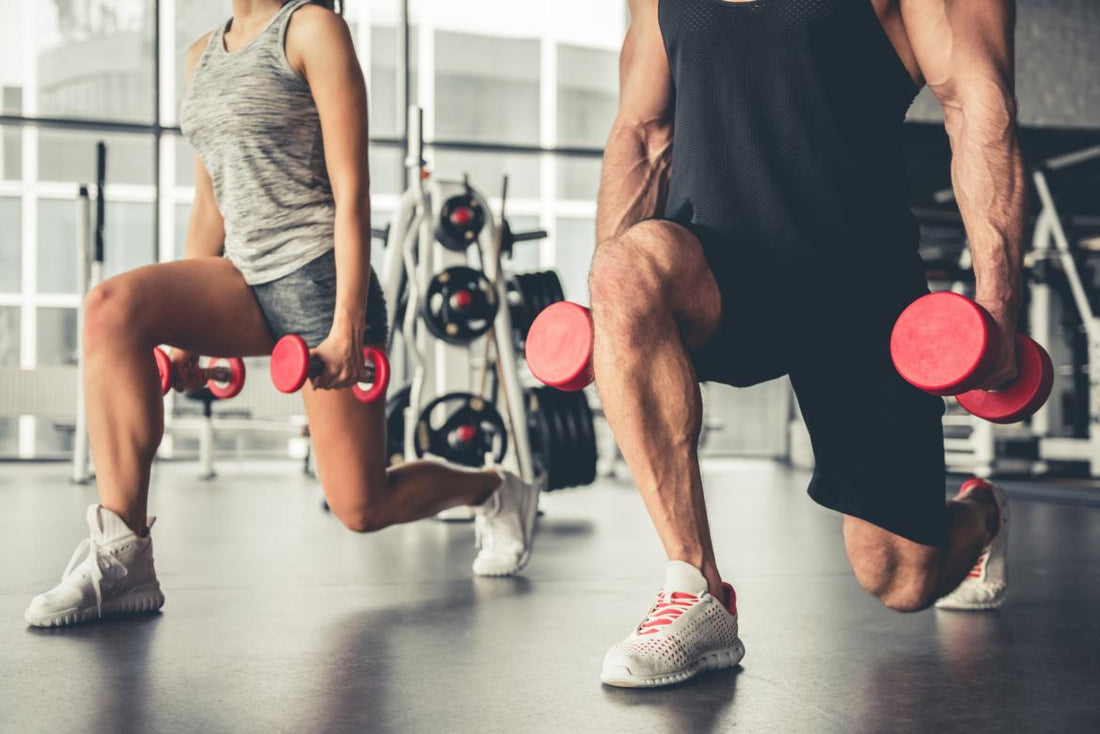 Couple doing lunges while holding red dumbbells in a gym. 