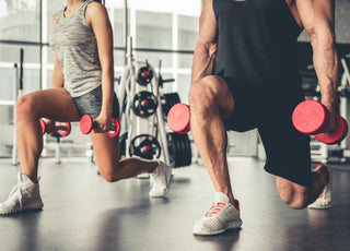 Couple doing lunges while holding red dumbbells in a gym. 