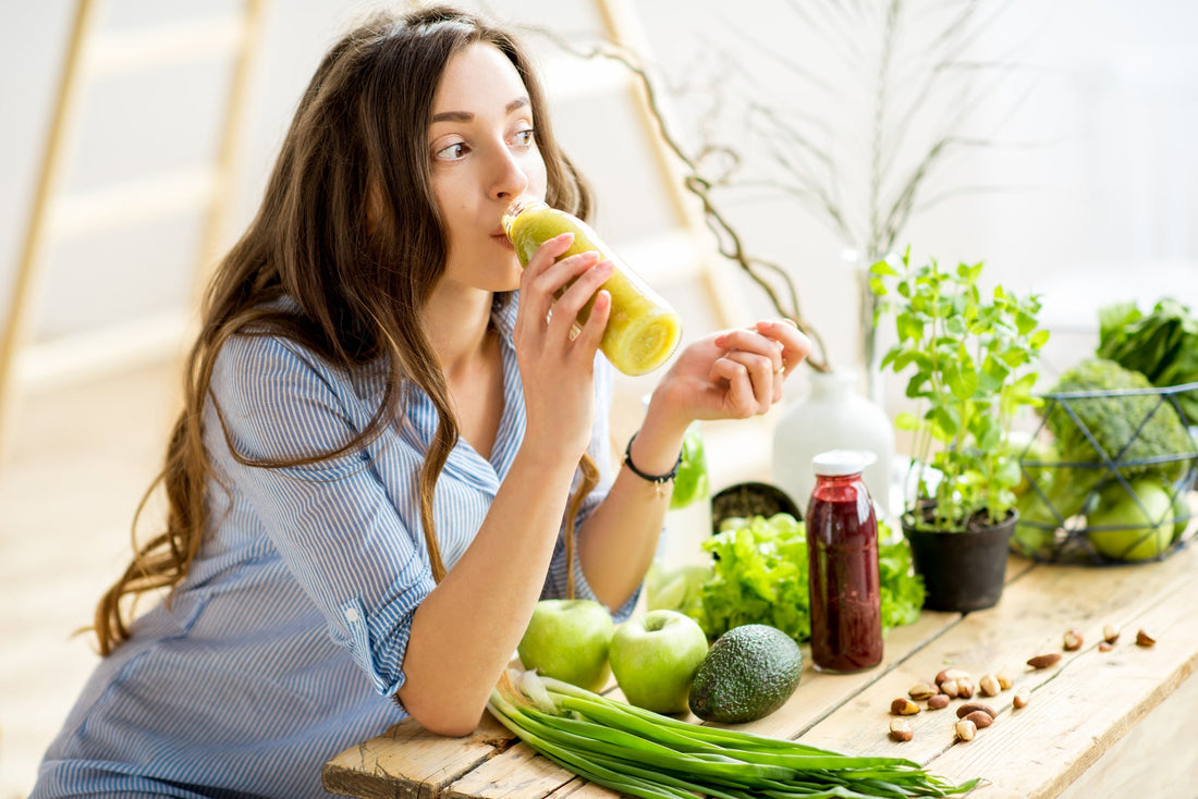 Woman leaning on her kitchen counter while drinking a healthy green drink. 