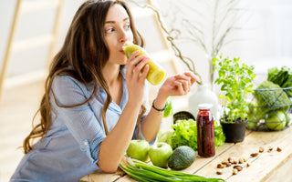 Woman leaning on her kitchen counter while drinking a healthy green drink. 