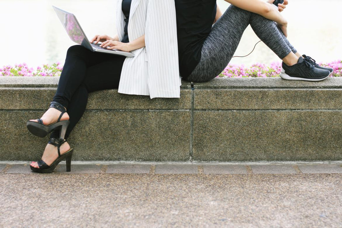 Concept of work-life balance as depicted by an image showing the same woman sitting back-to-back with herself. The version of her on the left shows her in business attire with a laptop while the version of her on the right is wearing workout gear.