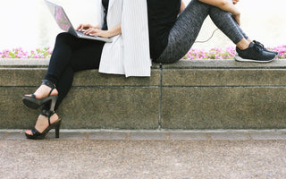 Concept of work-life balance as depicted by an image showing the same woman sitting back-to-back with herself. The version of her on the left shows her in business attire with a laptop while the version of her on the right is wearing workout gear.