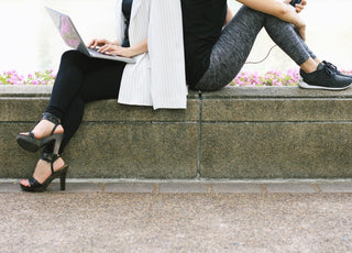 Concept of work-life balance as depicted by an image showing the same woman sitting back-to-back with herself. The version of her on the left shows her in business attire with a laptop while the version of her on the right is wearing workout gear.