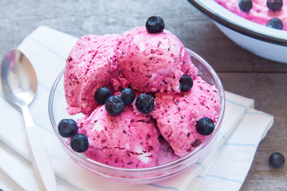 A glass bowl of pink ice cream topped with blueberries.