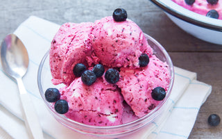 A glass bowl of pink ice cream topped with blueberries.