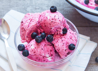 A glass bowl of pink ice cream topped with blueberries.