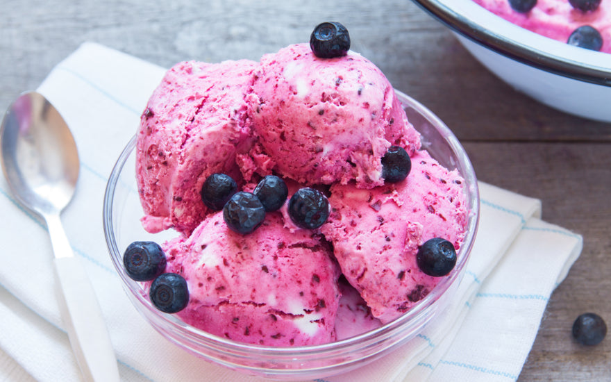 A glass bowl of pink ice cream topped with blueberries.