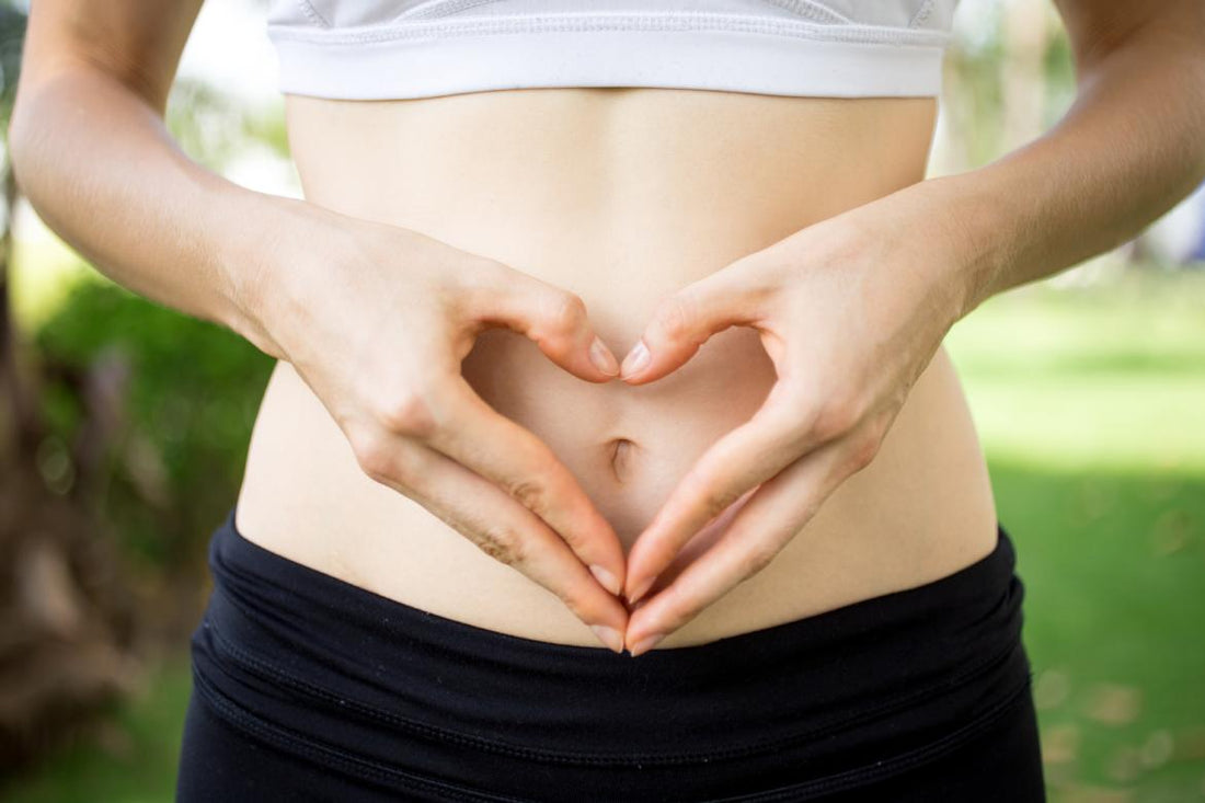Close up of female in workout gear holding her hands to form a heart over her belly button.