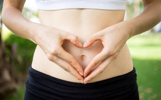 Close up of female in workout gear holding her hands to form a heart over her belly button.