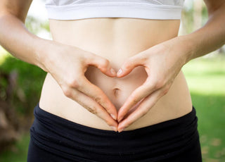 Close up of female in workout gear holding her hands to form a heart over her belly button.