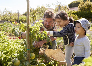 A man and two kids looking at a plant in the garden together.