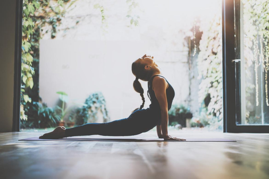 Young adult woman in a yoga pose on a mat in front of an open sliding glass door. 