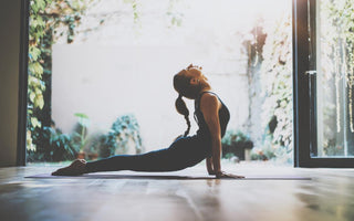 Young adult woman in a yoga pose on a mat in front of an open sliding glass door. 