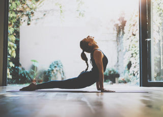 Young adult woman in a yoga pose on a mat in front of an open sliding glass door. 