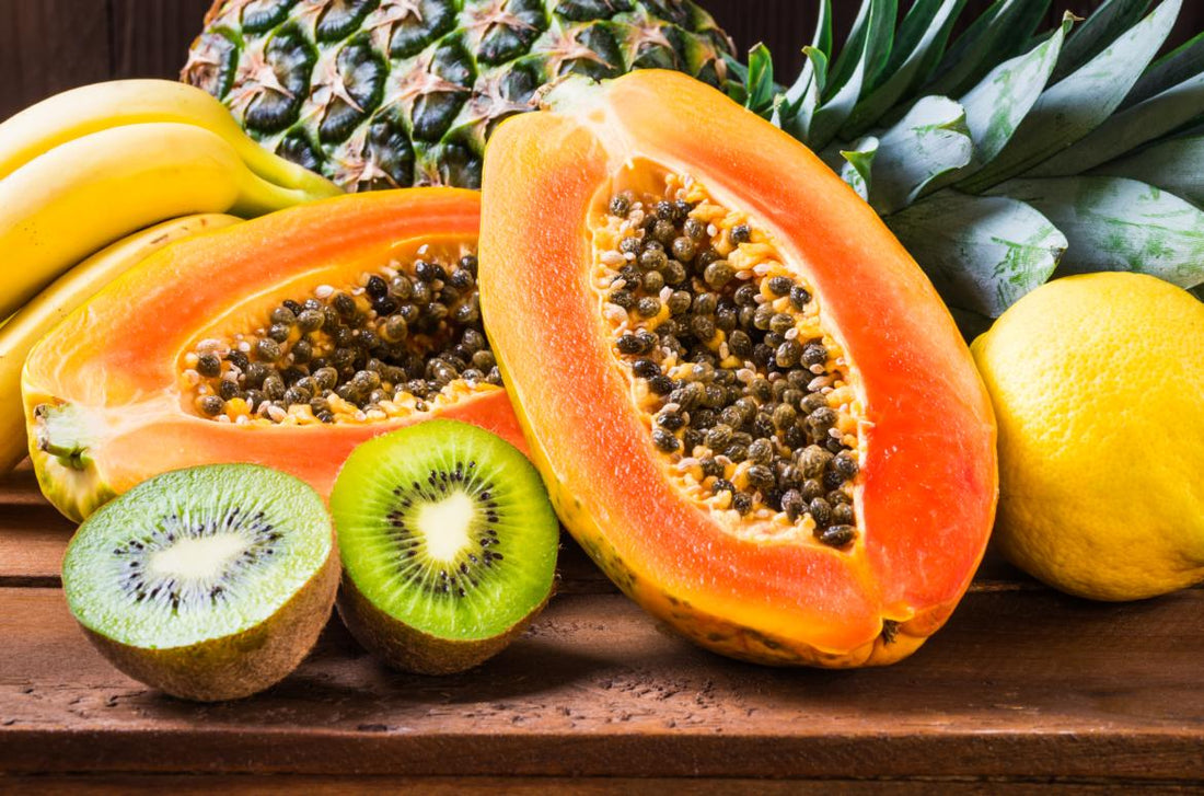Close up of a papaya and kiwi cut in half and laid on a wooden table. 