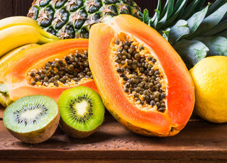 Close up of a papaya and kiwi cut in half and laid on a wooden table. 