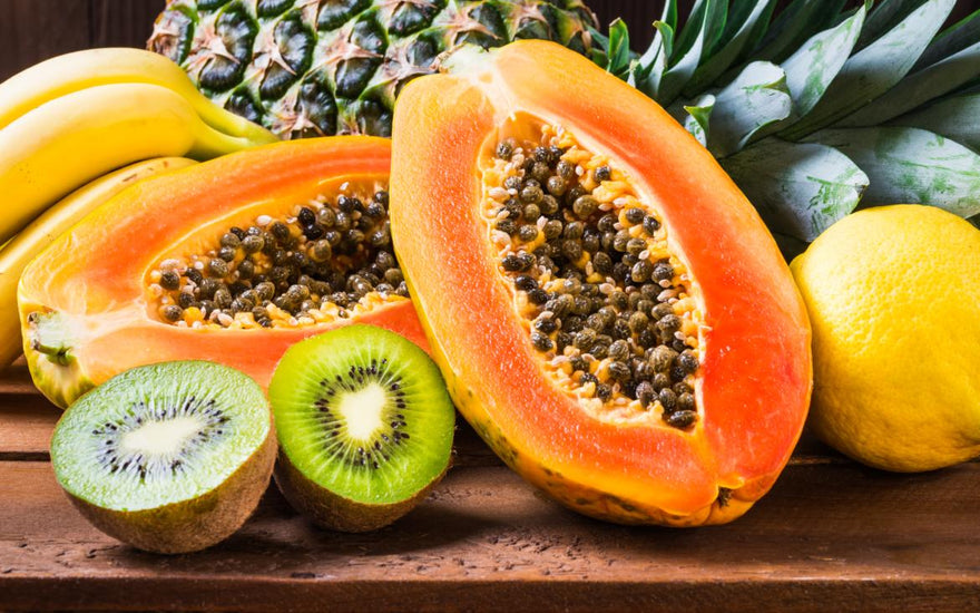 Close up of a papaya and kiwi cut in half and laid on a wooden table. 