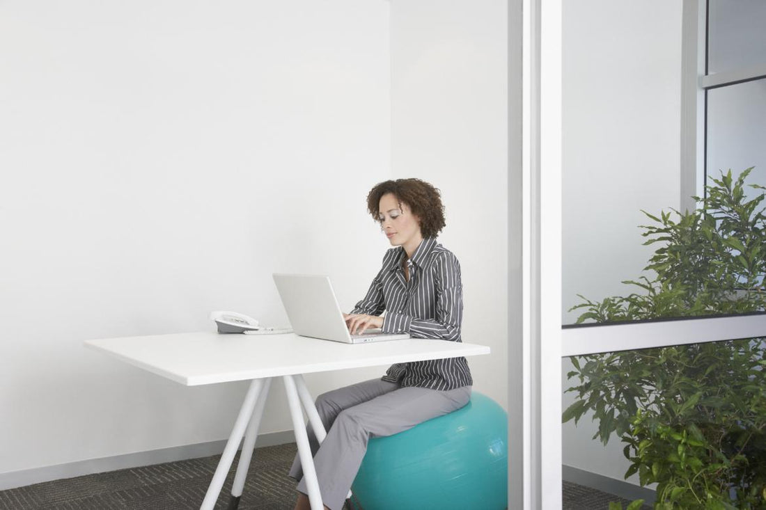 Business woman sitting on an exercise ball at her desk while she works on her laptop.