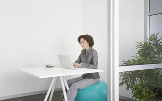 Business woman sitting on an exercise ball at her desk while she works on her laptop.