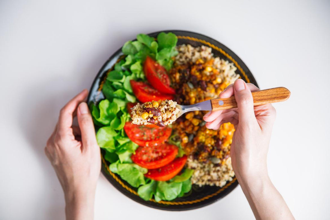 Top-down view of a vegan dinner bowl sitting on a table with a woman's hand using a fork to scoop a bite out of the bowl. 