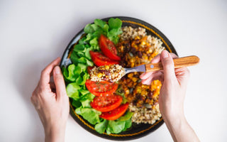 Top-down view of a vegan dinner bowl sitting on a table with a woman's hand using a fork to scoop a bite out of the bowl. 