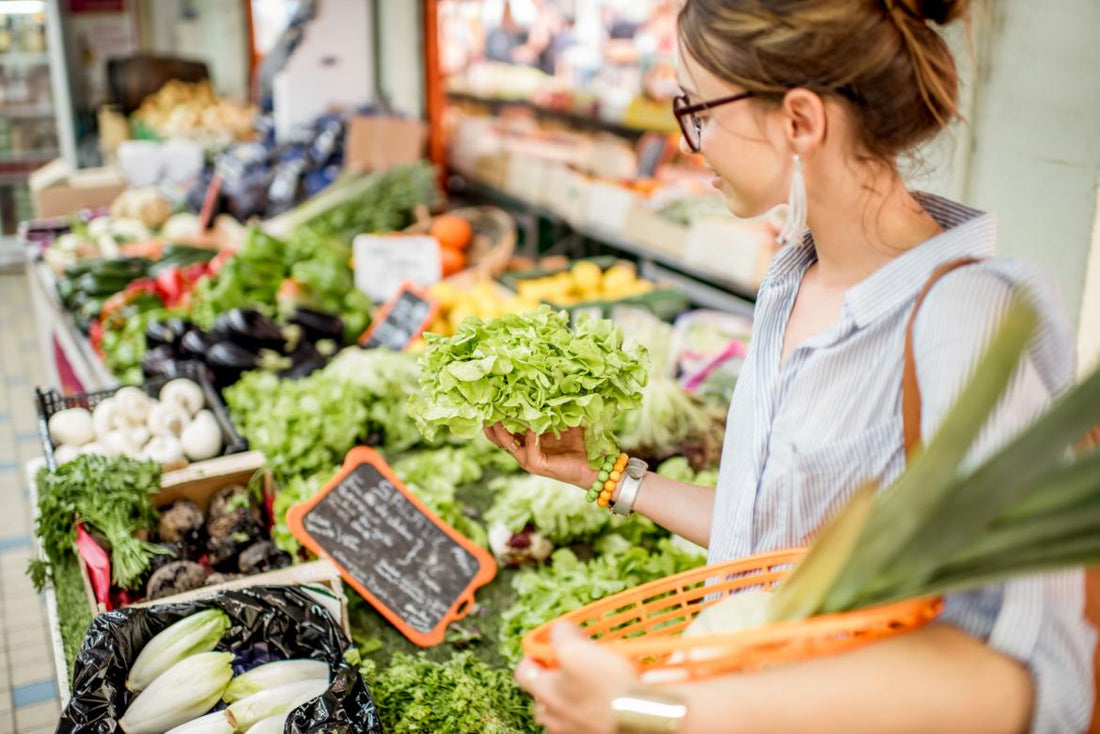 Adult woman examining greens in the produce section of a grocery store.