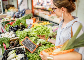 Adult woman examining greens in the produce section of a grocery store.