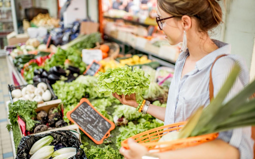 Adult woman examining greens in the produce section of a grocery store.