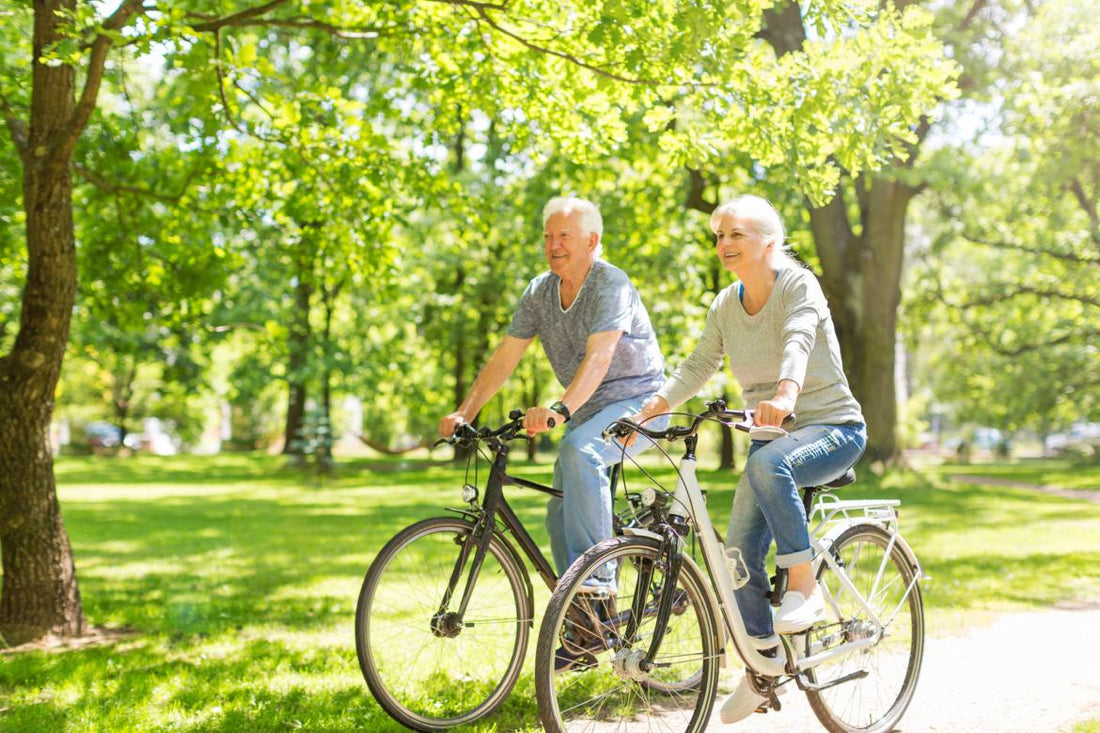Elderly couple riding bikes on a path through a park.