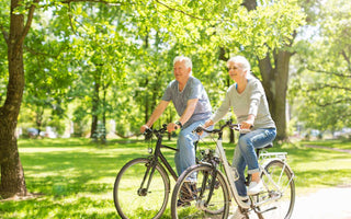 Elderly couple riding bikes on a path through a park.