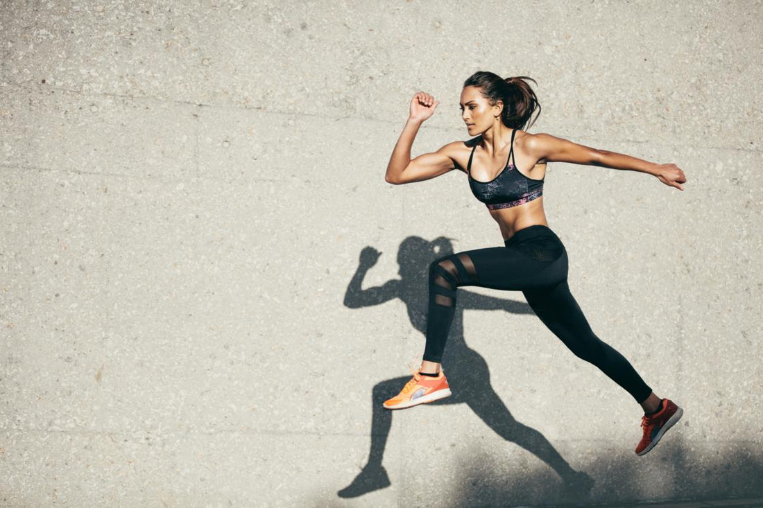 Woman in all black workout gear mid-jump during her outdoor workout. 