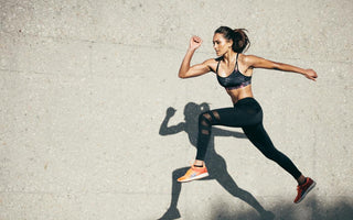 Woman in all black workout gear mid-jump during her outdoor workout. 