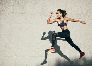 Woman in all black workout gear mid-jump during her outdoor workout. 