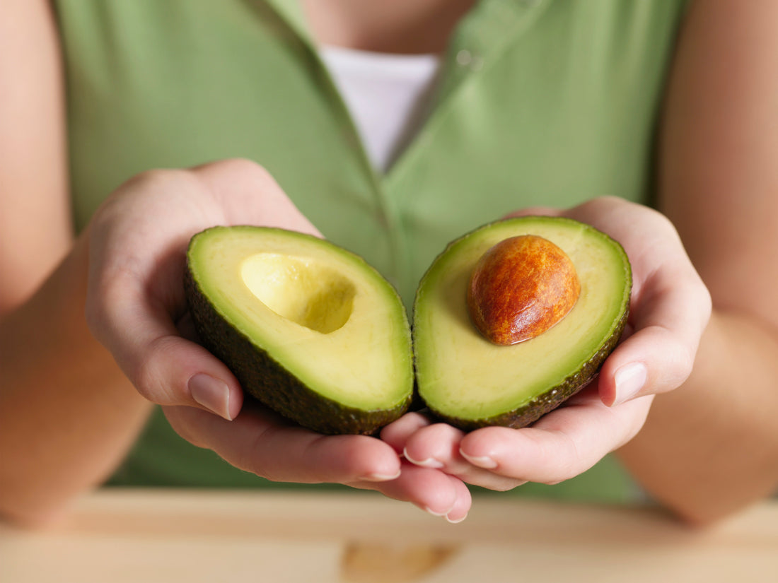 Woman in a green shirt holding two halves of an avocado in her hands.