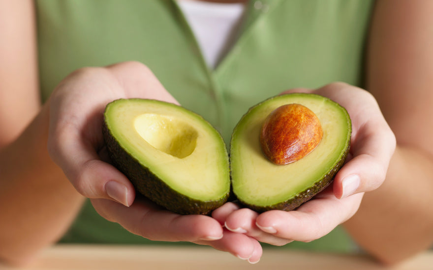 Woman in a green shirt holding two halves of an avocado in her hands.