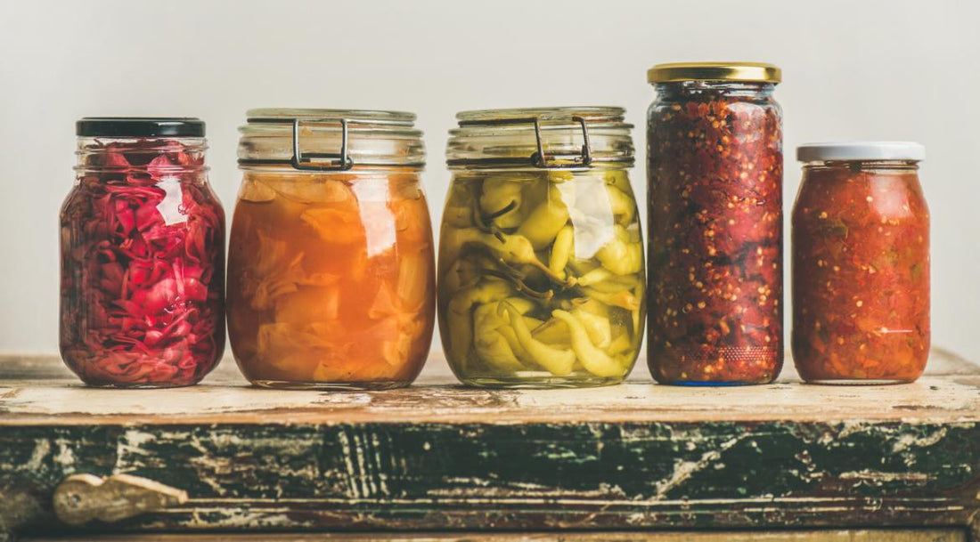 Five jars of various fermented foods sitting on a wooden counter. 