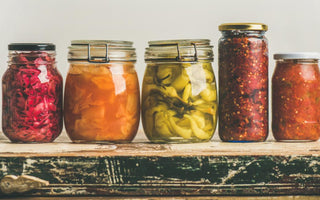 Five jars of various fermented foods sitting on a wooden counter. 