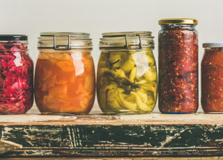 Five jars of various fermented foods sitting on a wooden counter. 