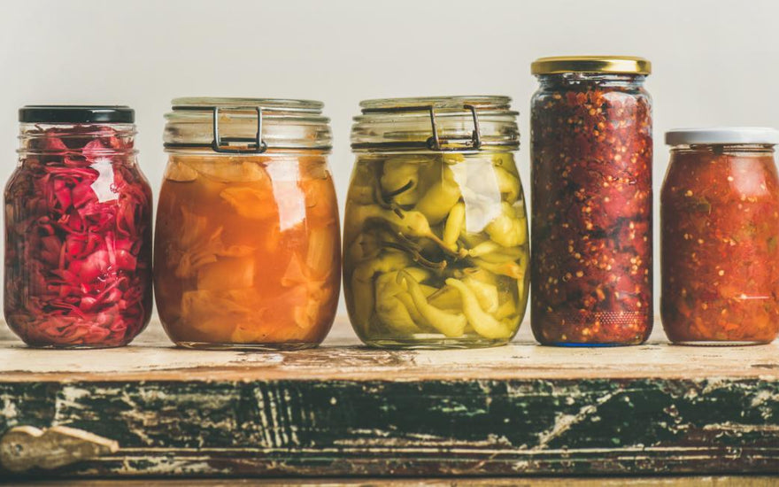 Five jars of various fermented foods sitting on a wooden counter. 